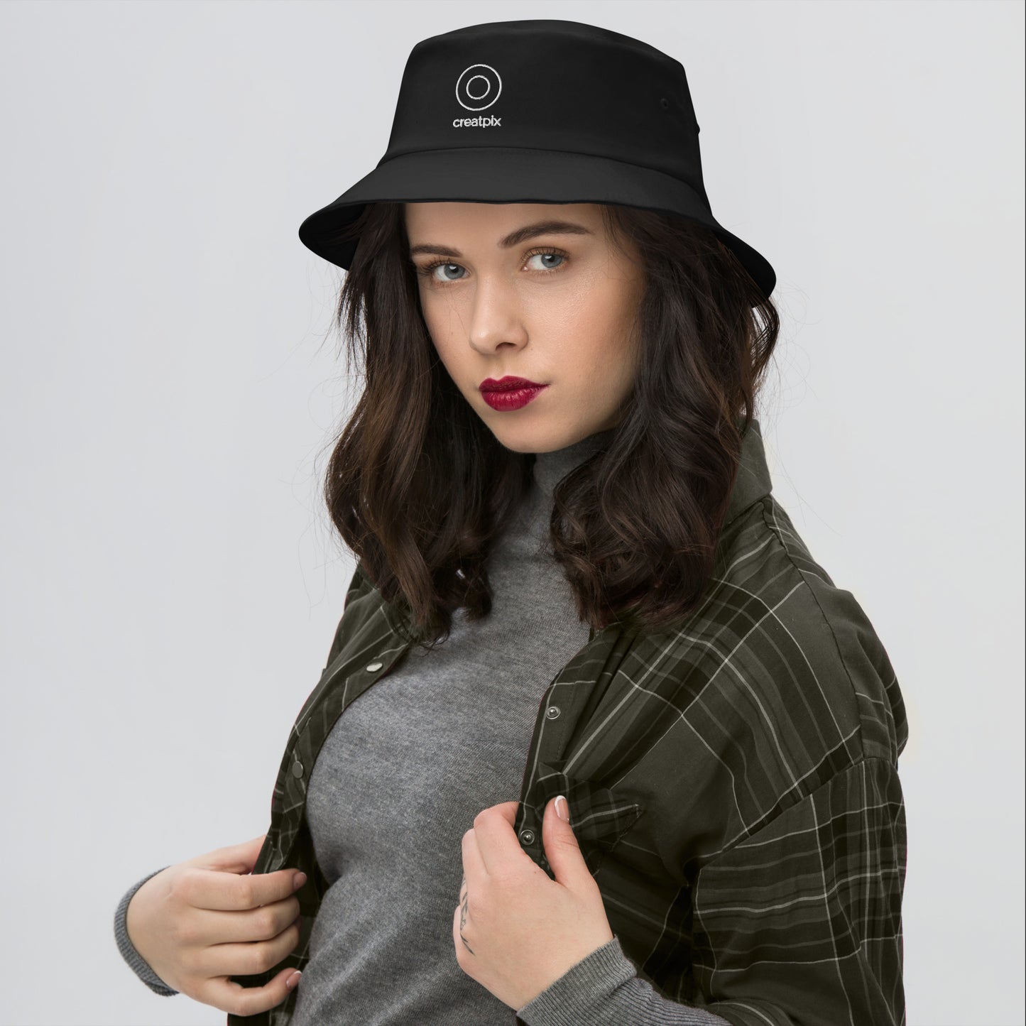Model wearing the Creatpix classic minimal black bucket hat with its white embroidered circle logo, paired with a modern plaid shirt