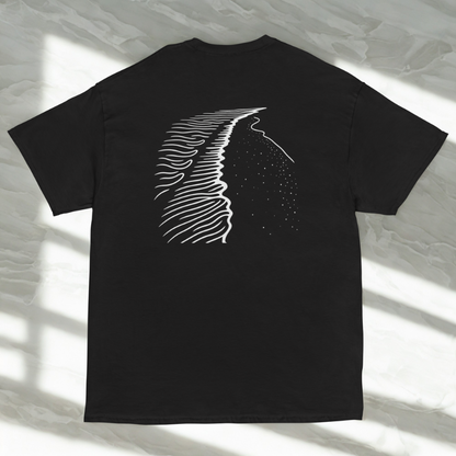 Back view of charcoal tee with white shoreline linework and dotted sea, soft window shadows on pale marble.