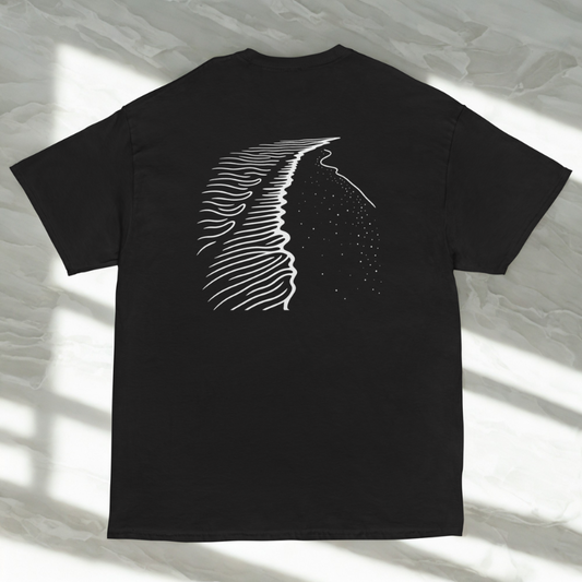 Back view of charcoal tee with white shoreline linework and dotted sea, soft window shadows on pale marble.