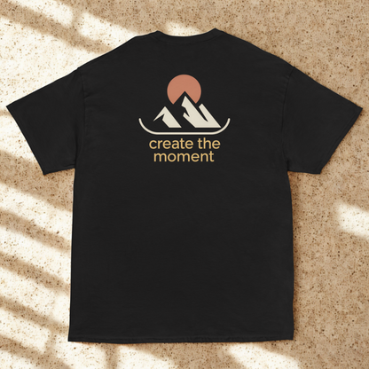 Back view of charcoal tee with minimalist twin peaks and sun icon and “create the moment” slogan, soft dappled window shadows on terrazzo.