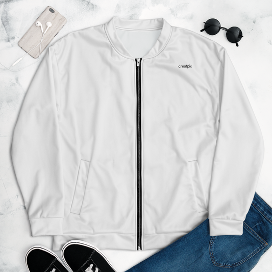 Flat-lay front view of white bomber jacket with small chest wordmark and black zipper, styled with phone, earbuds, sunglasses, jeans and sneakers on light marble surface.