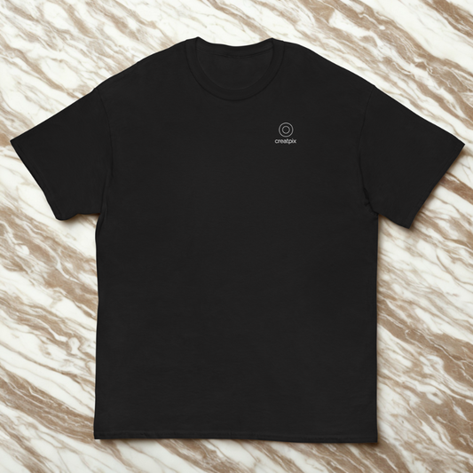 Front view of charcoal tee with small circle logo and “creatpix” at left chest, brown-white marble backdrop.