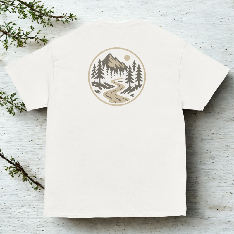 Back view of white tee with small round badge showing a river winding through evergreen forest, clean neutral backdrop.