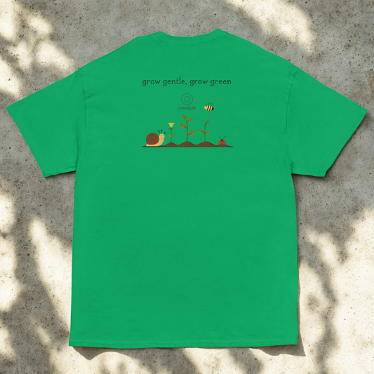 Back view of green tee with tiny garden illustration and line quote, sunlit flat-lay near foliage.