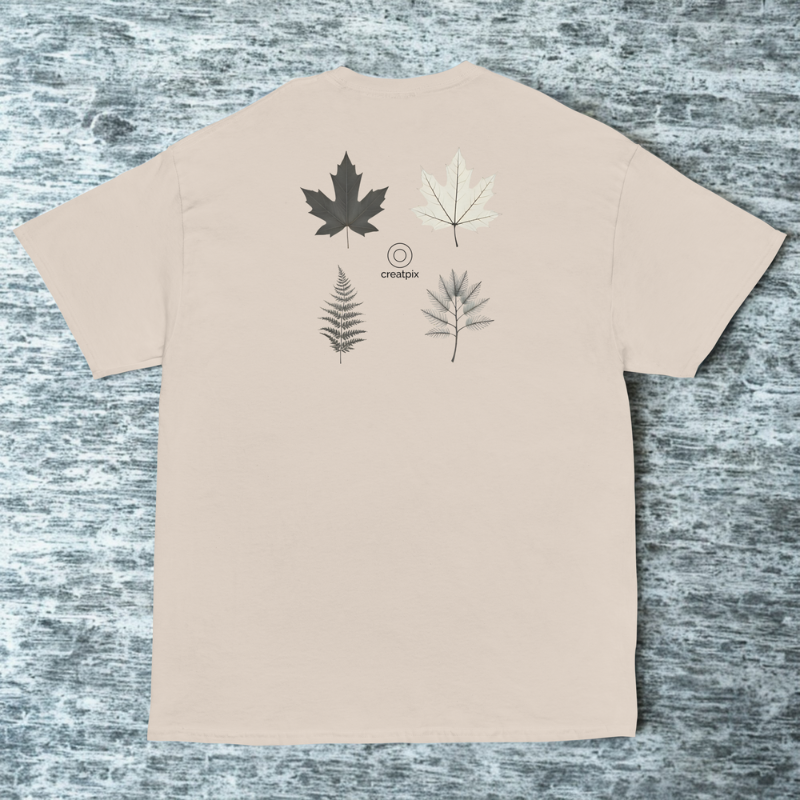 Back view of beige tee with four botanical leaf sketches above small creatpix logo, cool stone surface.