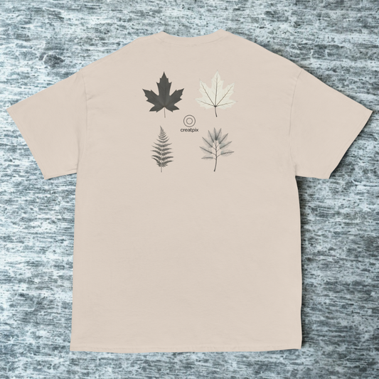 Back view of beige tee with four botanical leaf sketches above small creatpix logo, cool stone surface.