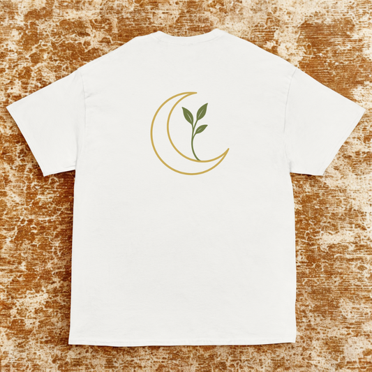 Back view of white tee with gold crescent moon and green sprouting leaves, warm distressed rug backdrop.
