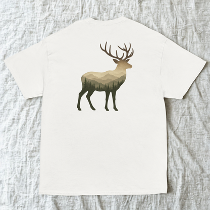 Back view of white tee with deer silhouette set against mountain peaks, light wood surface.
