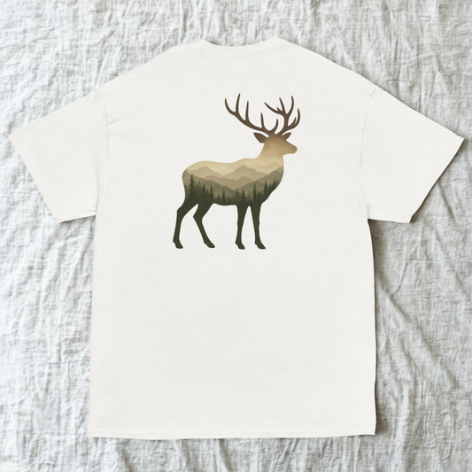 Back view of white tee with deer silhouette set against mountain peaks, light wood surface.