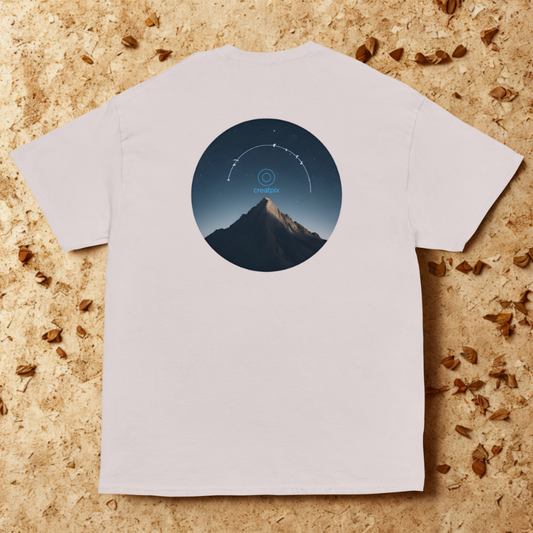 Back view of grey tee with circular night mountain graphic and star arc, styled on natural wood.