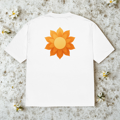 Back view of white tee with large orange sunrise-blossom graphic, soft shadows on pale concrete.