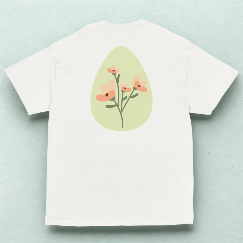 Back view of white tee with soft green oval and peach wildflower stems, pale mint fabric backdrop.