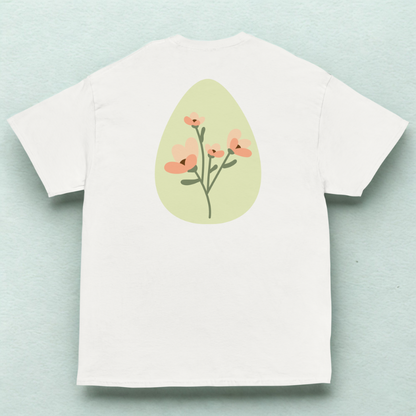 Back view of white tee with soft green oval and peach wildflower stems, pale mint fabric backdrop.