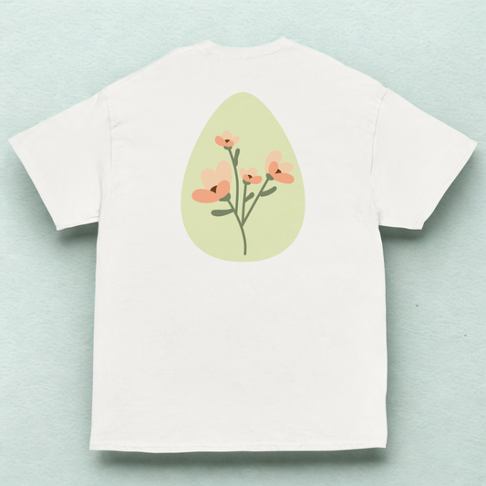 Back view of white tee with soft green oval and peach wildflower stems, pale mint fabric backdrop.