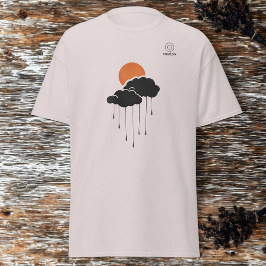 Front view of sand tee with orange sun and dark rain cloud graphic with falling lines, small creatpix chest mark, rustic wood backdrop with pinecones.