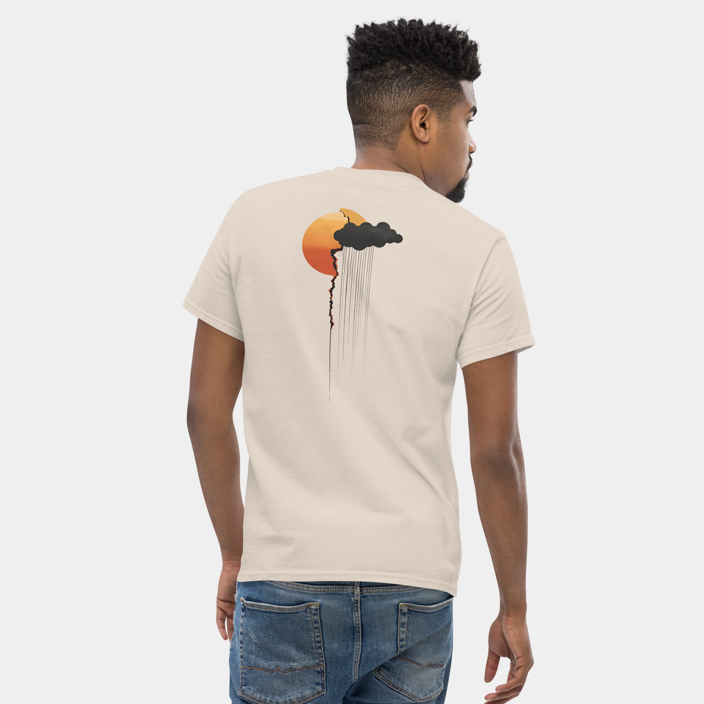 On-model back view wearing sand tee with sun-and-cloud rain graphic placed high on the back, clean studio wall.