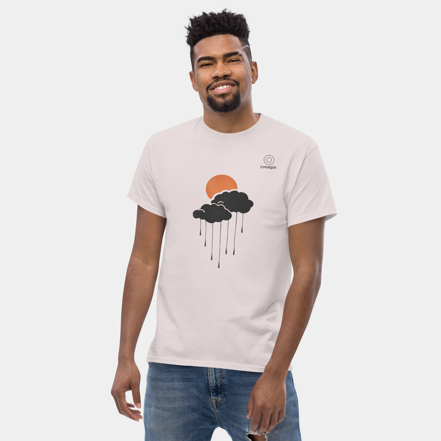 On-model front view wearing sand tee with sun-and-cloud rain graphic, casual studio setting.