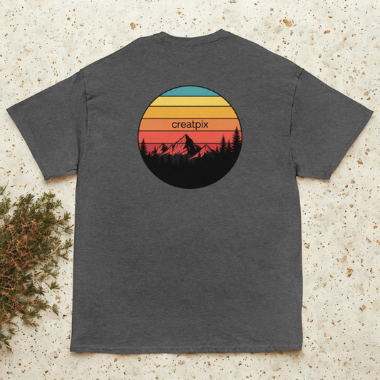 Back view of charcoal tee with retro sunset stripes and mountain silhouette circle, pine sprigs nearby.