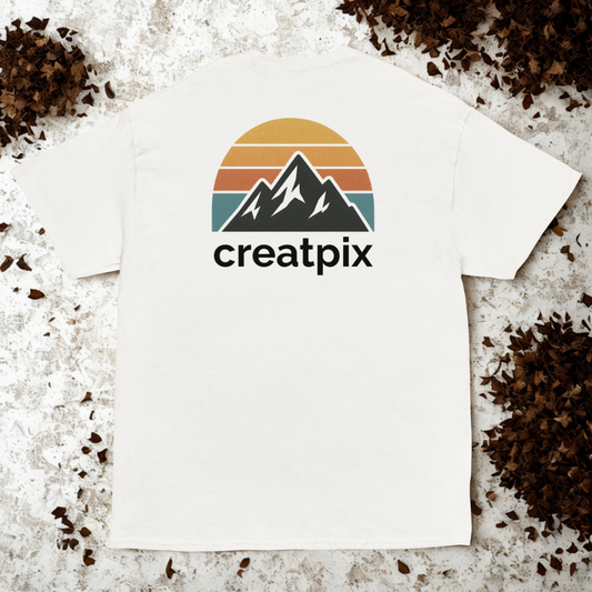Back view of white tee with retro sunset stripes and mountain silhouette above wordmark, dried leaves scattered around edges.