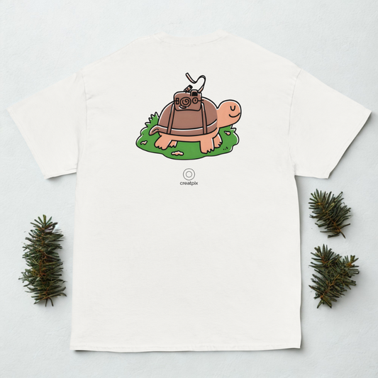Back view of white tee with cute turtle carrying a camera illustration, styled with small pine sprigs.