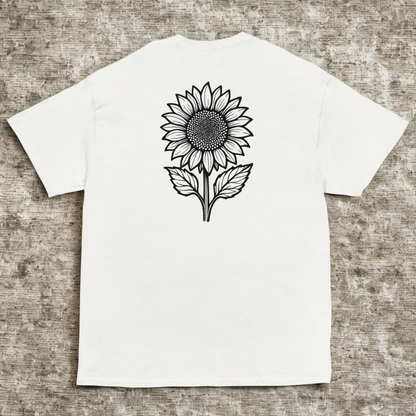 Back view of white tee with black sunflower line art and leaves, cool stone texture background.