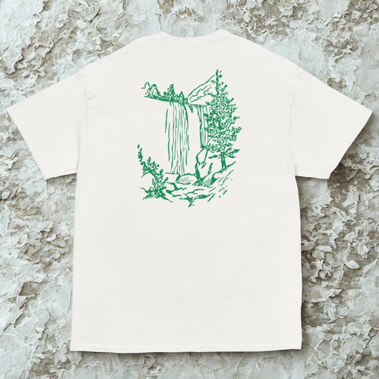 Back view of white tee with green line-drawn cliff and waterfall scene, textured stone background.